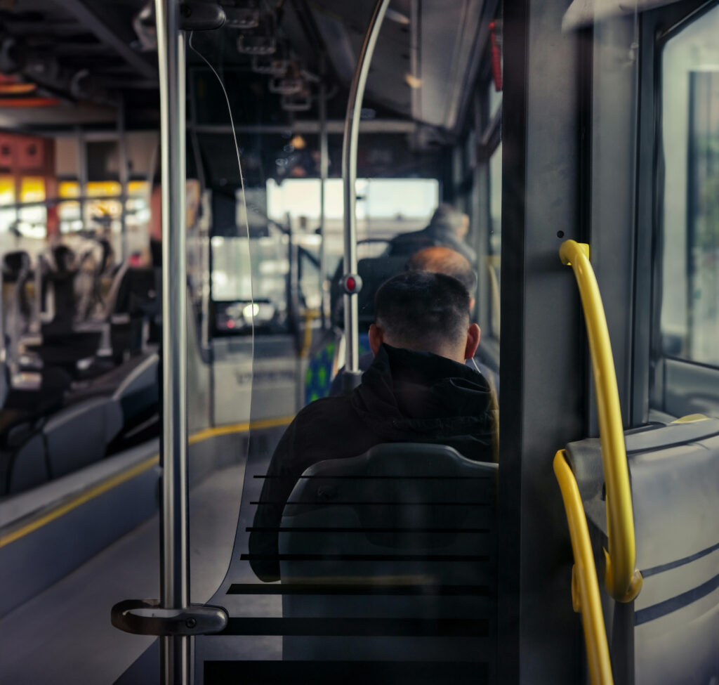 Passenger seen from behind, seated beside a bus window.