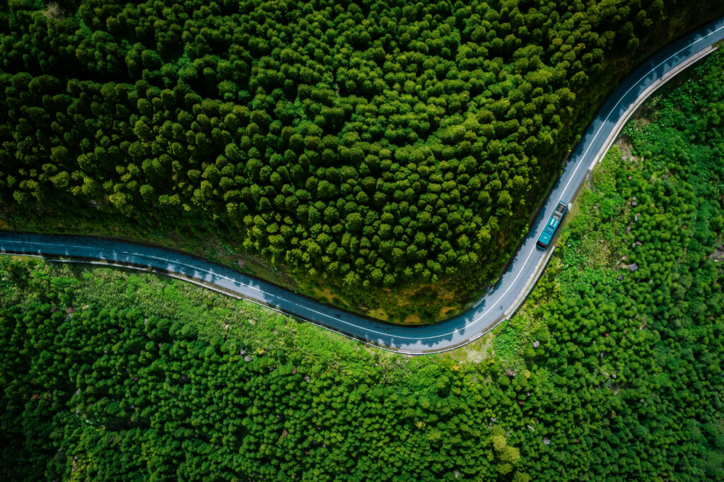 Aerial view of a bus on a winding road surrounded by dense green forest.