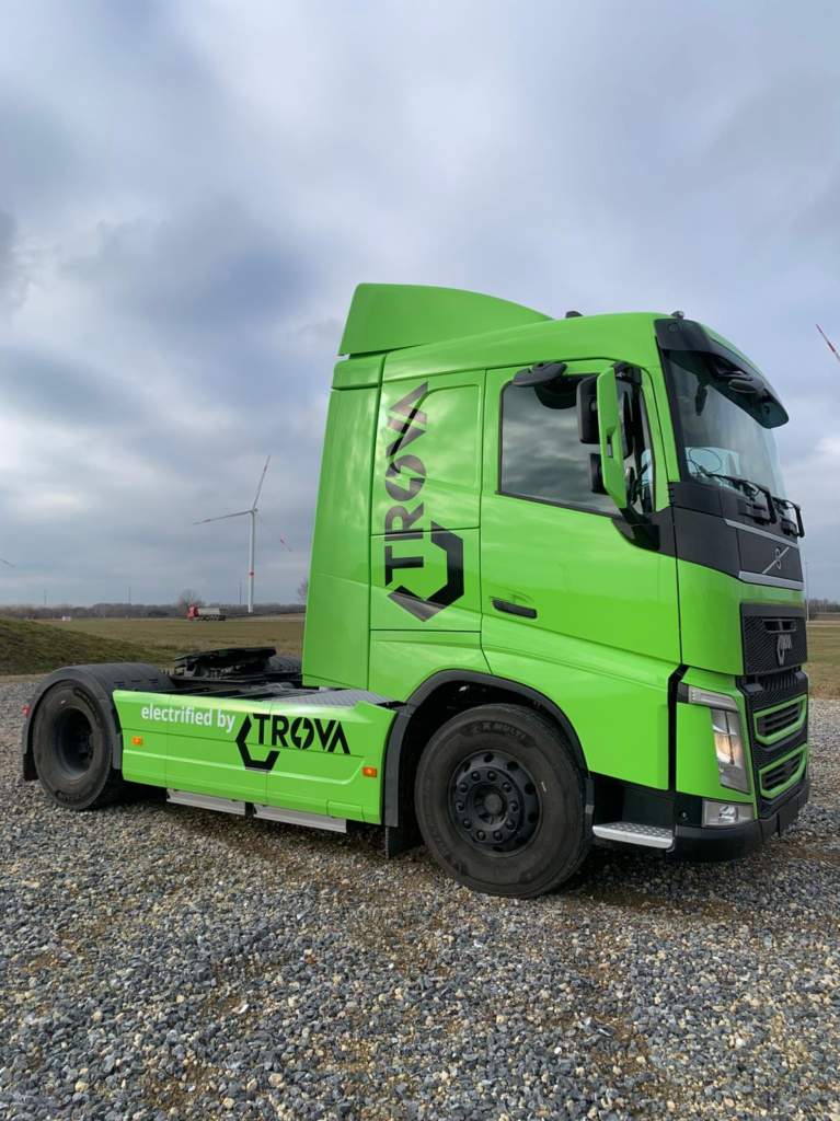 Green Trova truck viewed from the front on a road lined with trees.